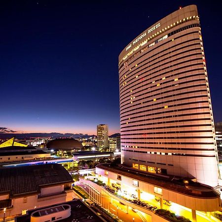Kobe Portopia Hotel Exteriér fotografie The photo shows a tall, modern hotel building illuminated at night. The hotel's facade features large windows and a sleek design, with lights illuminating its structure. In the foreground, there are some smaller buildings or structures, with a view o