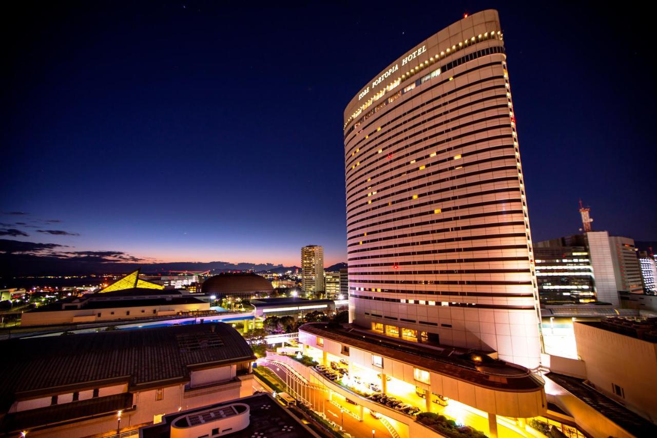 Kobe Portopia Hotel Exteriér fotografie The photo shows a tall, modern hotel building illuminated at night. The hotel's facade features large windows and a sleek design, with lights illuminating its structure. In the foreground, there are some smaller buildings or structures, with a view o