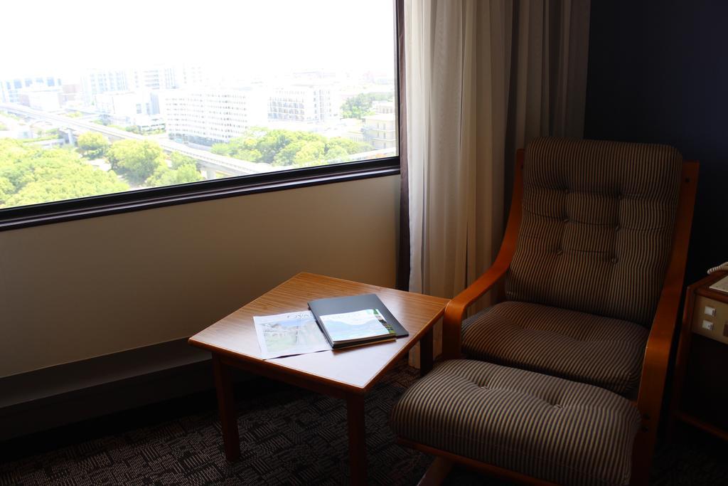 Kobe Portopia Hotel Exteriér fotografie The image depicts a cozy corner of a room featuring a comfortable chair next to a small wooden table. The chair has a cushioned back and seat, and is positioned near a large window that offers a view of the outdoors, which is not fully visible. On th