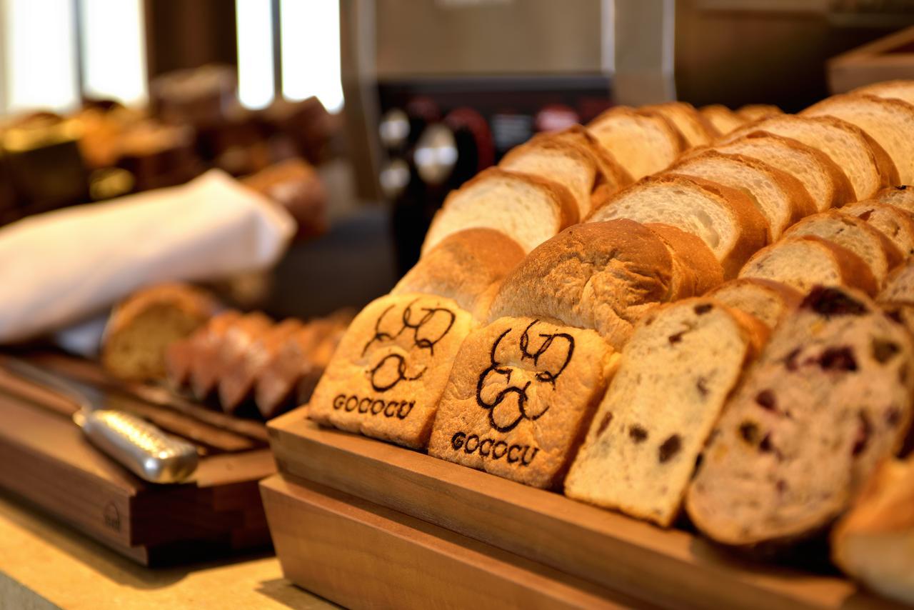 Kobe Portopia Hotel Exteriér fotografie The image shows a display of various types of bread arranged neatly on a wooden serving tray. There are slices of bread, including some that appear to be toasted, and at least one slice features a decorative imprint with the word "GOOCCU." The backgr