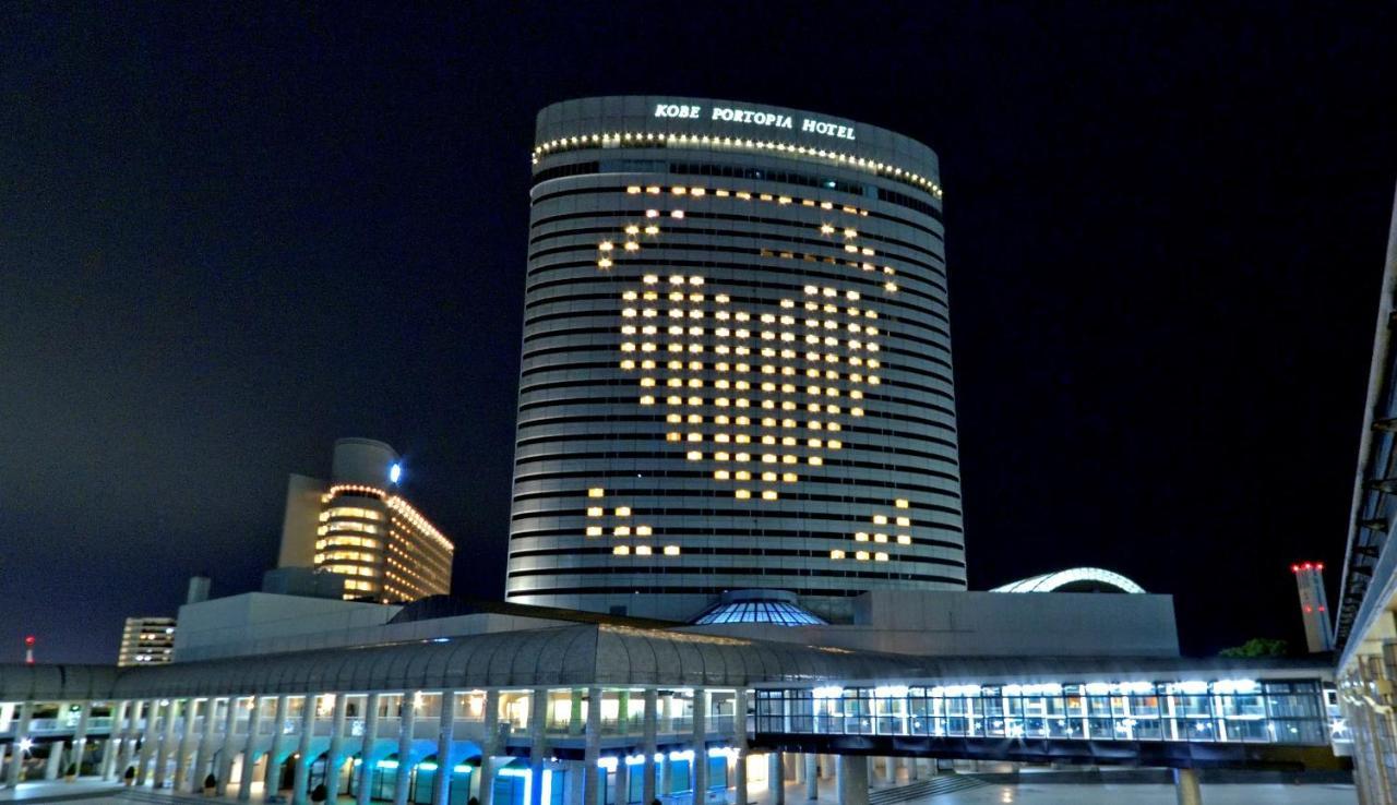 Kobe Portopia Hotel Exteriér fotografie The photo shows a large hotel building at night, with illuminated windows forming a heart shape on its facade. The hotel is labeled as "Kobe Portopia Hotel." In the foreground, there is a structure that appears to be part of the hotel complex, along 